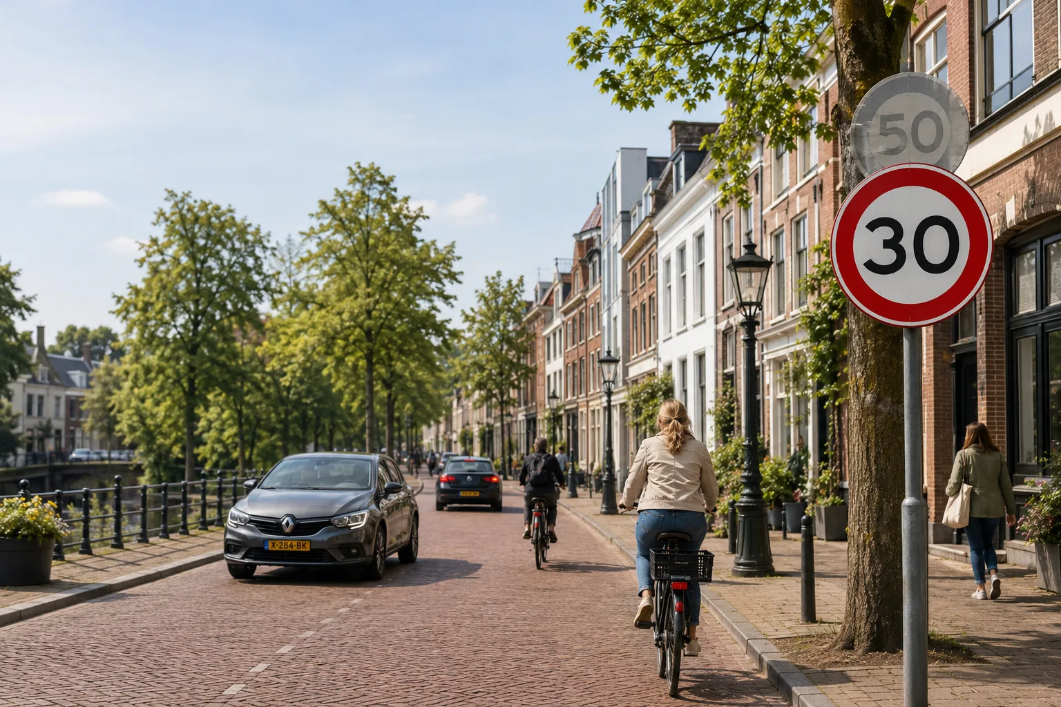 A Utrecht street shared by cyclists and cars, with a new 30 km/h speed-limit sign replacing the previous 50 km/h limit.