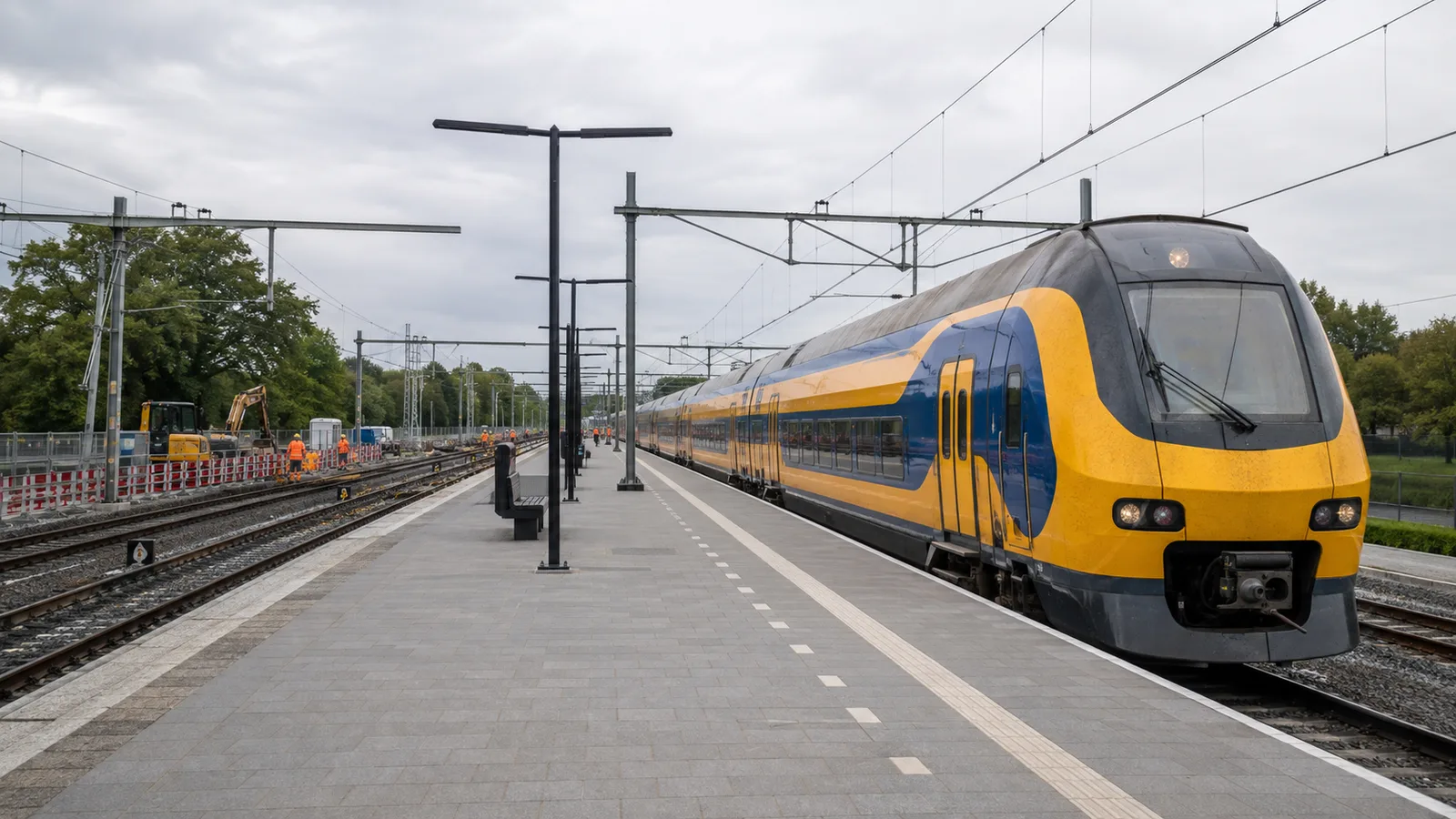 A yellow and blue intercity train beside a platform while railway crews work on nearby tracks.